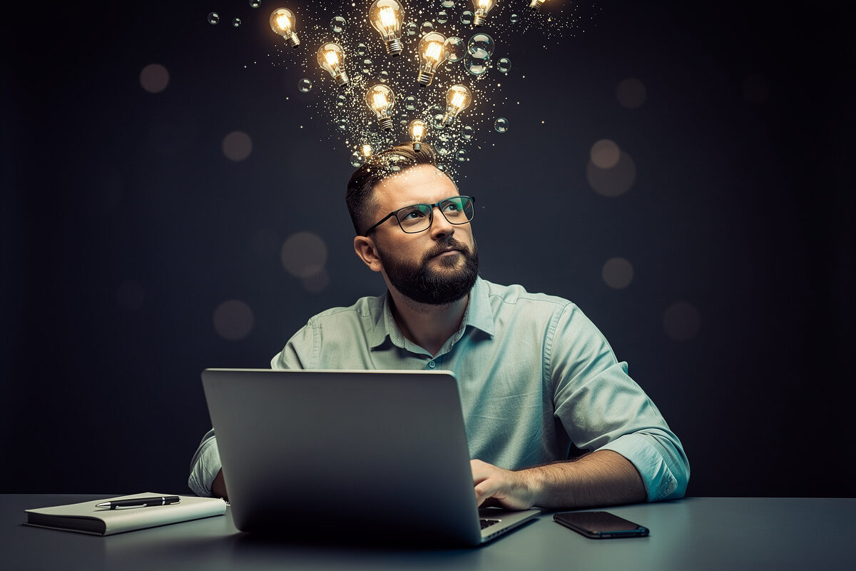 Web designer pensieroso con idee luminose che emergono dalla mente mentre lavora al laptop